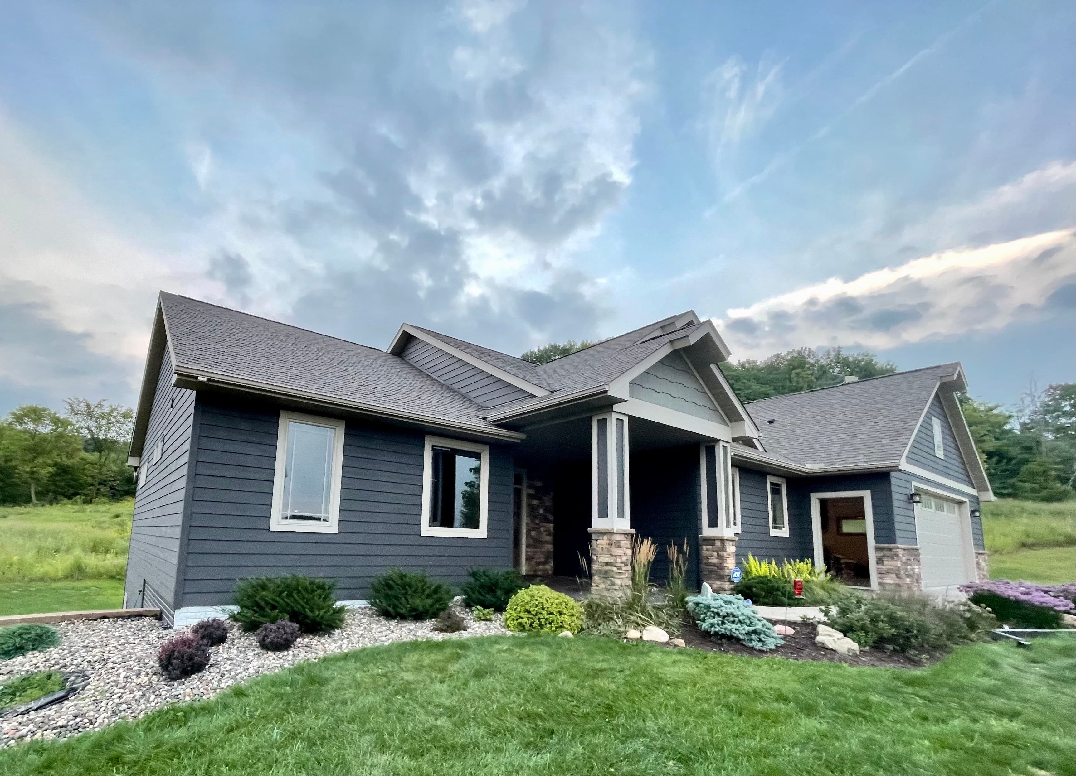 Modern gray house with stone accents and landscaped yard under a cloudy sky.