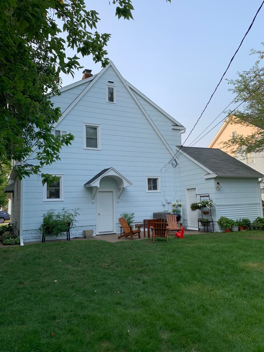 Light blue house with backyard seating area and greenery on a sunny day.