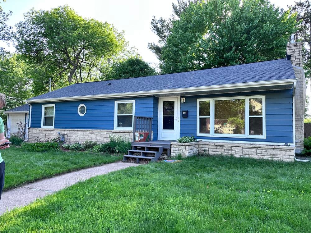 Blue single-story house with stone accents, large front windows, and green lawn.