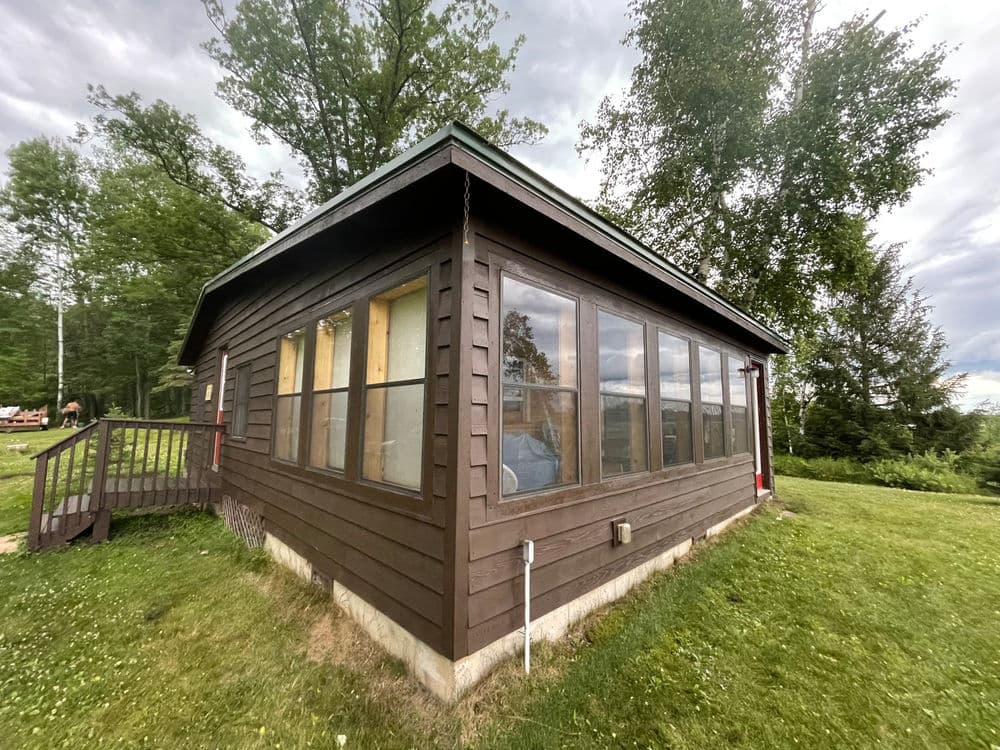 Wooden cabin with large windows, surrounded by greenery and trees, ideal for nature retreats.